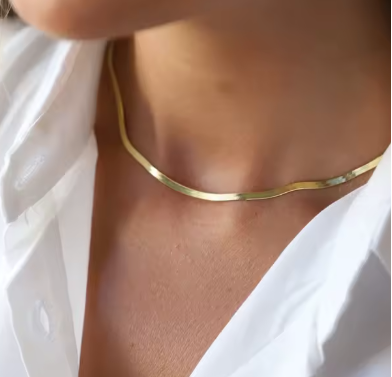 Gold shiny herringbone necklace worn by a woman with a white shirt